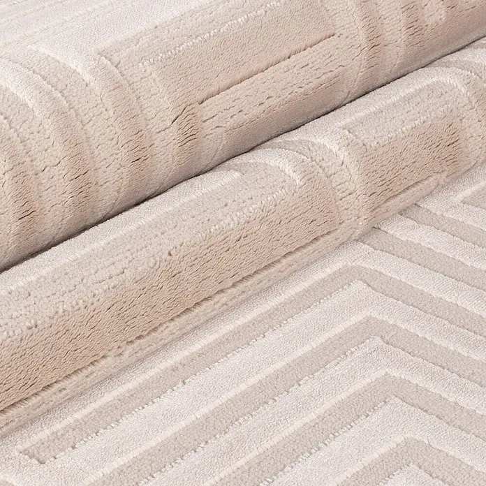 Kurzflorteppich Sahara III - Beige, 170 x 120 cm, 100 % Polypropylen - Detailaufnahme eines gerollten, beigen Teppichs mit geometrischem Muster. Die Textur des Teppichs ist weich und einladend.