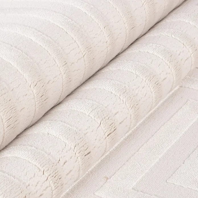 Kurzflorteppich Sahara V - Creme, 200 x 140 cm, 100 % Polypropylen - Nahaufnahme eines gerollten, cremefarbenen Teppichs mit einem dezenten geometrischen Muster, das Textur und Komfort vermittelt.