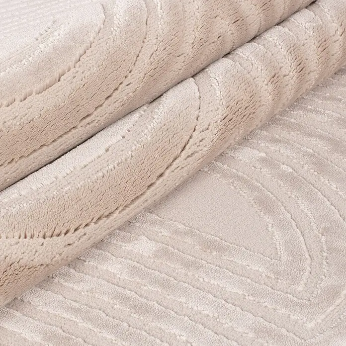 Kurzflorteppich Sahara II - Beige, 170 x 120 cm, 100 % Polypropylen - Nahaufnahme eines gerollten, beigen Teppichs mit einem subtilen, gewellten Muster. Textur und Farbton des Teppichs stehen im Fokus.