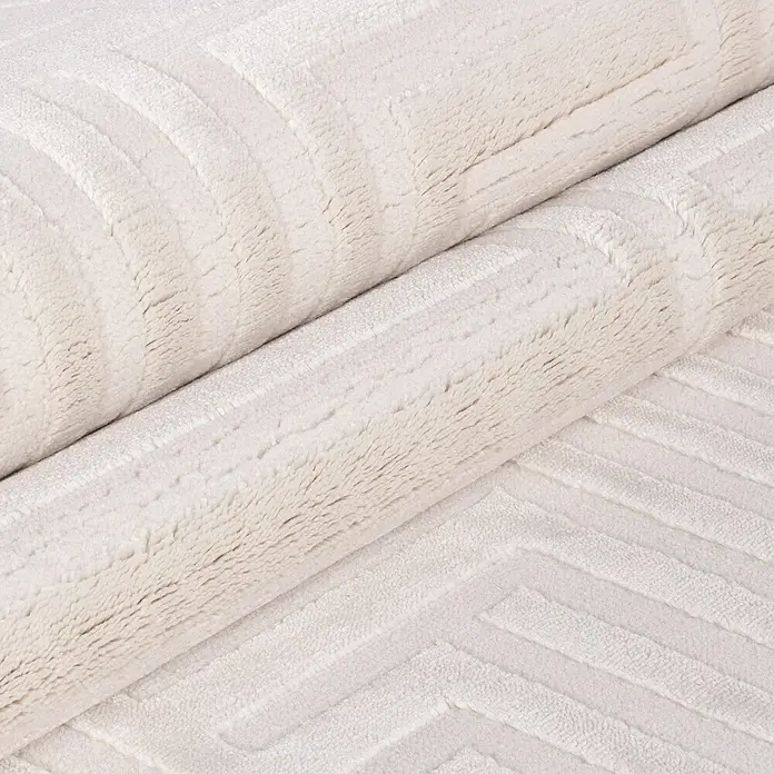 Kurzflorteppich Sahara III - Creme, 170 x 120 cm, 100 % Polypropylen - Detailansicht eines gerollten, weißen Teppichs mit geometrischem Muster. Die weiche Textur und das subtile Design sind gut erkennbar.