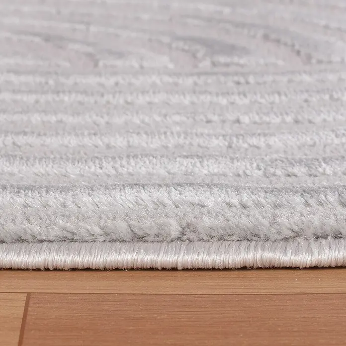 Kurzflorteppich Sahara I - Silber, 250 x 80 cm, 100 % Polypropylen - Nahaufnahme eines grauen Teppichs mit einem subtilen Muster, der auf einem Holzboden liegt. Der Teppich hat eine weiche Textur und eine saubere Kante.