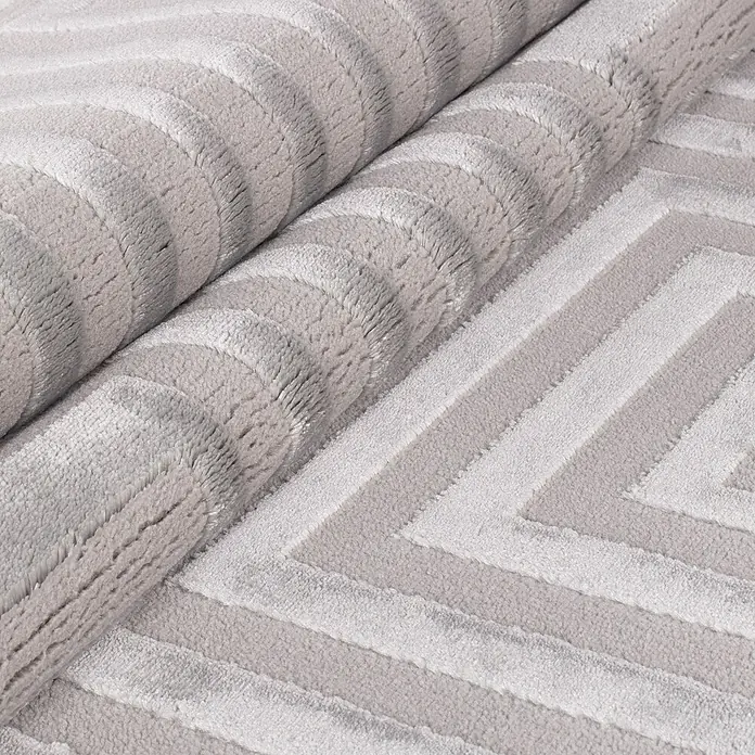 Kurzflorteppich Sahara V - Silber, 340 x 240 cm, 100 % Polypropylen - Nahaufnahme eines gerollten, hellgrauen Teppichs mit geometrischen Mustern und weicher Textur.