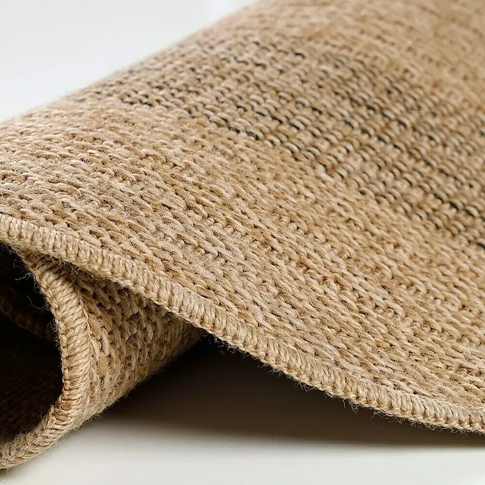 Outdoor-Teppich Comilla I - Schwarz, Durchmesser: 80 cm, 100 % Polypropylen - Detailaufnahme eines gewebten Teppichs mit brauner Textur, der aufgerollt ist und die feinen Details der Verarbeitung zeigt.