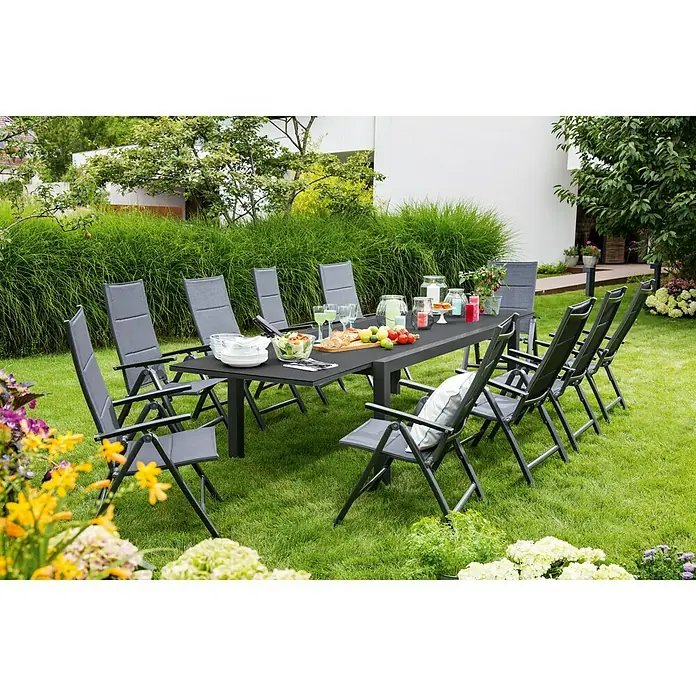 Sunfun Maja Garten-Positionssessel - Anthrazit, Klappbar - Gartenset mit Esstisch und Stühlen auf einer grünen Wiese, umgeben von Blumen und Pflanzen. Ideal für Mahlzeiten im Freien.