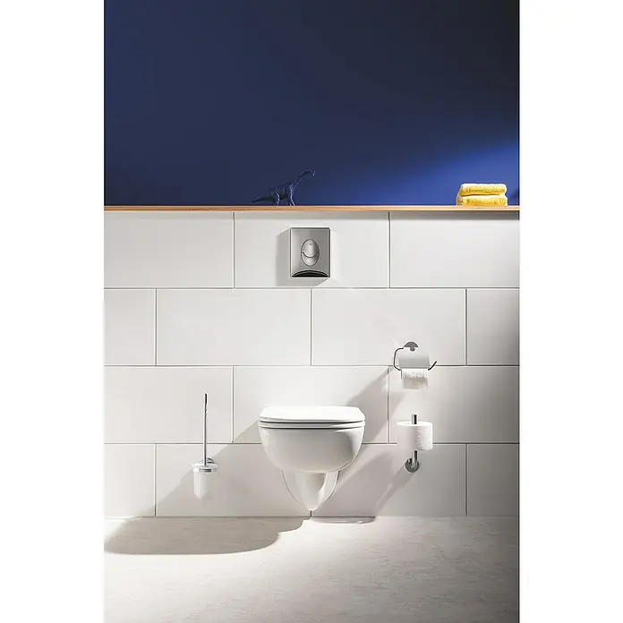 Grohe Start Betätigungsplatte - Chrom, 2-Mengen-Spülung - Dieses Bild zeigt eine moderne, wandhängende Toilette mit integriertem Spülkasten vor einer weissen Flieswand. Darüber ein Holzregal mit Deko.