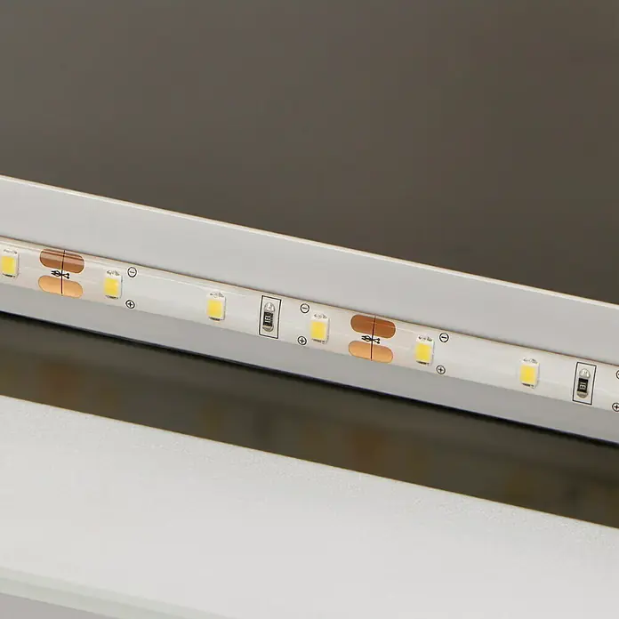 DSK Lichtspiegel Silver Shine 2.0 - 140 x 70 cm - Nahaufnahme einer LED-Leiste mit kleinen LEDs, Kupferkontakten und Symbolen zur Polaritätsanzeige, eingebaut in einem weißen Profil.