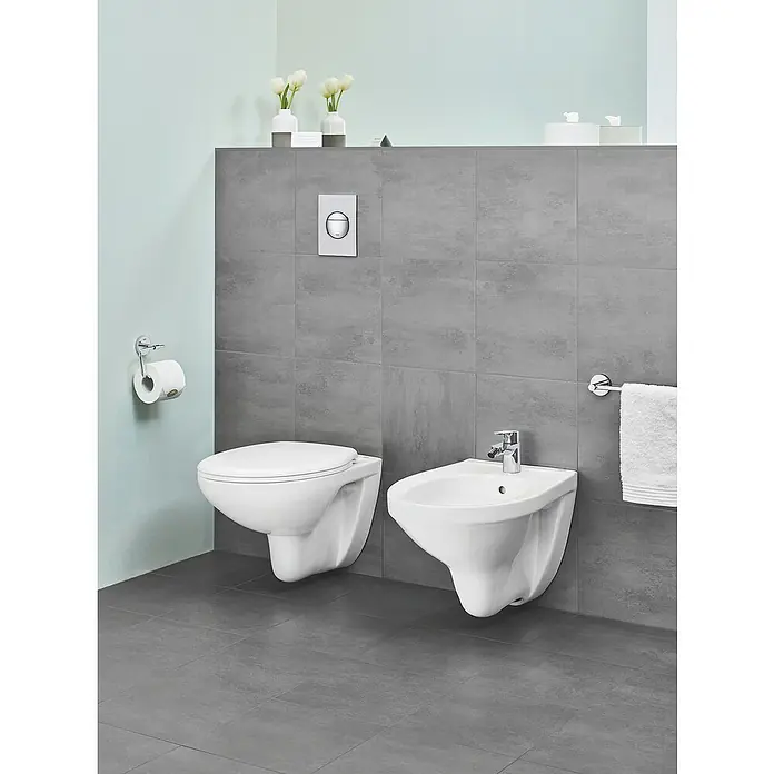 Grohe Bidetarmatur - Glänzend - Das Bild zeigt eine moderne Badezimmerinstallation mit einer wandhängenden Toilette und einem Bidet vor einer grauen Wand.