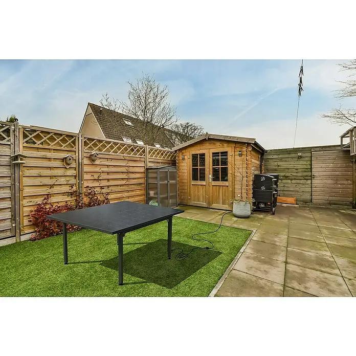 Technaxx Solar-Tischkraftwerk 400 W TX-250 - 400 W, L x B x H: 173 x 114 x 84 cm - Eine Nahaufnahme eines modernen schwarzen Gartentisches auf einem grünen Rasen mit einem Gartenhaus und einer Holzwand im Hintergrund.