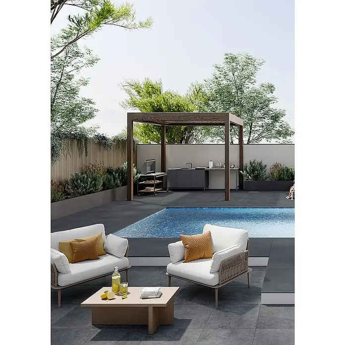 Art-Tec by Palazzo Terrassenfliese60 x 60 x 2 cm, Graphit, Matt - Helle Sessel mit Kissen um einen Couchtisch im Freien, neben einem Pool und einer Outdoor-Küche mit Holzrahmen.