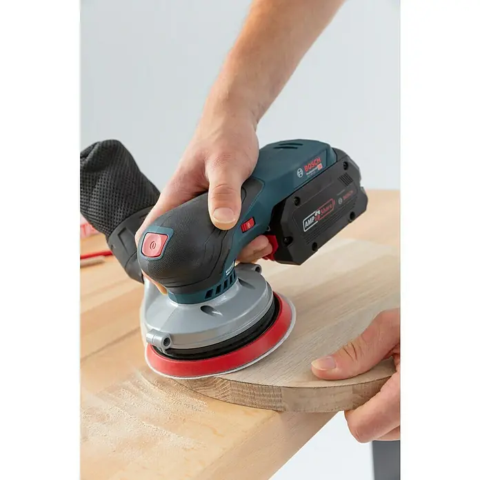 Bosch Professional AMPShare 18V Akku-Exzenterschleifer GEX 18V-125 - 18 V, Ohne Akku, Durchmesser Schleifteller: 125 mm, Kunststoffkoffer - Ein Akku-Exzenterschleifer von Bosch wird zum Schleifen eines Holzstücks verwendet. Dieses Werkzeug ist ideal für präzise Schleifarbeiten.