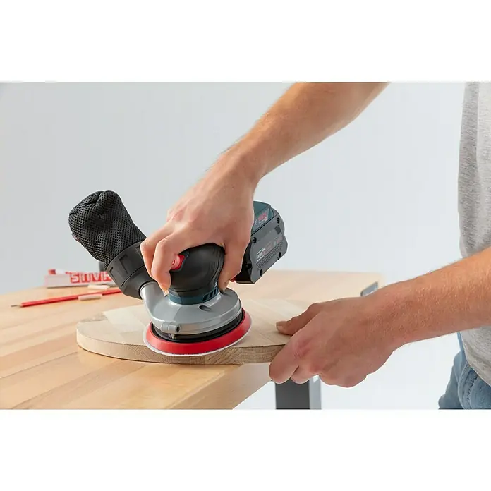 Bosch Professional AMPShare 18V Akku-Exzenterschleifer GEX 18V-125 - 18 V, Ohne Akku, Durchmesser Schleifteller: 125 mm, Kunststoffkoffer - Nahaufnahme eines Mannes, der mit einem Bosch Exzenterschleifer ein Holzstück bearbeitet, wobei der Schleifer und die Holzoberfläche im Fokus stehen.