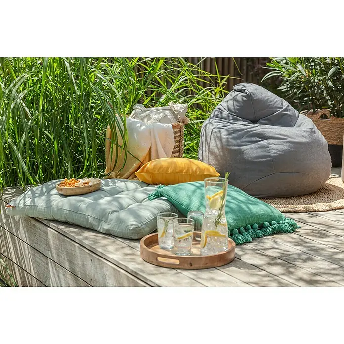 Kissen Kucuri - Grün, 45 x 45 cm, 100 % Baumwolle - Entspannte Outdoor-Szene mit einem grauen Sitzsack, Kissen und einem Tablett mit Erfrischungen auf einer Holzterrasse.