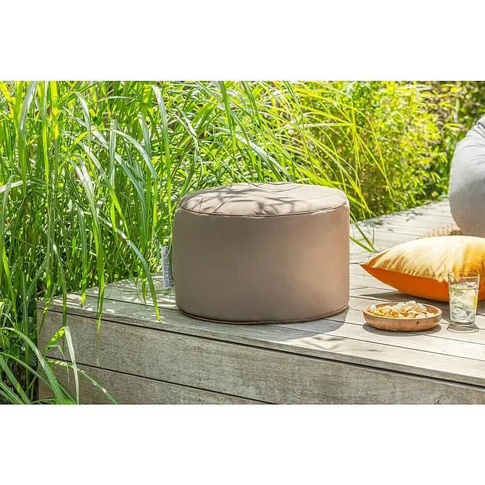 Sitting Point Sitzhocker Dotcom Jamie - Ø x H: 50 x 30 cm, Braun, 100 % Polyester - Ein beiger Sitzhocker steht auf einer Holzterrasse neben einem Getränk und einem Snack. Perfekt für entspannte Stunden im Freien.