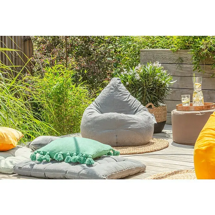 Kissen Kucuri - Grün, 45 x 45 cm, 100 % Baumwolle - Gemütliche Outdoor-Lounge-Ecke mit einem grauen Sitzsack und bunten Kissen auf einer Holzterrasse, umgeben von üppigem Grün.