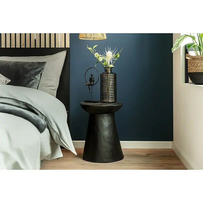 LOGOCLIC Sockelleiste Weiß - 260 cm x 17 mm x 70 mm, MDF, Weiß, Einseitig gerundet - Ein Nachttisch in dunkler Steinoptik mit einer geriffelten Vase und einer Dekofigur mit Ring, neben einem eleganten Bett.