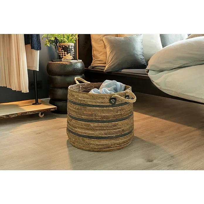 Manta para sofá Happy - 150 x 200 cm, Negro - Una cesta de lavandería tejida con asas de fibra natural está sentada en un piso de madera clara en un dormitorio.