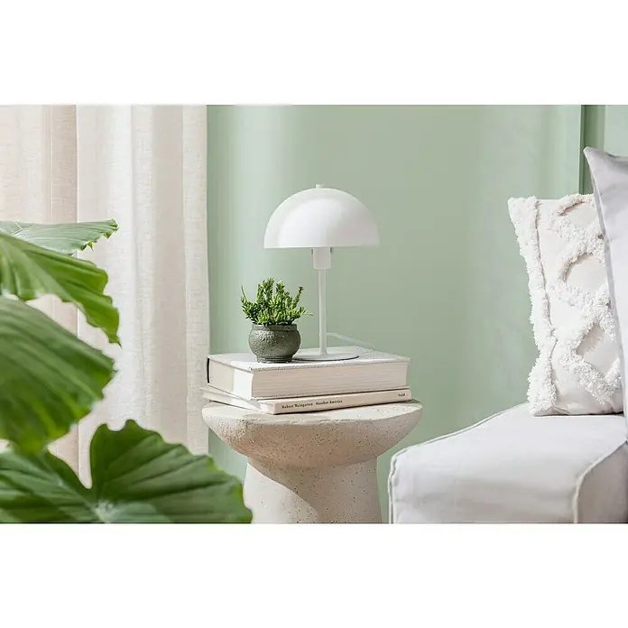 Elbersdrucke Schlaufenbandschal PureB x H: 140 x 255 cm, 100 % Polyester, Weiß - Nahaufnahme einer weißen Tischleuchte auf einem Beistelltisch mit Büchern und einer Pflanze, die eine gemütliche Atmosphäre erzeugt.