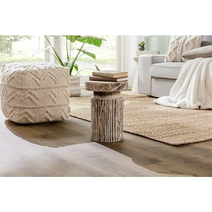 Juteteppich Nature 502 - Naturbraun, 290 x 200 cm, 100 % Jute - Ein beiger Pouf mit Zickzackmuster und ein Beistelltisch aus Holz mit zwei Büchern darauf, die eine gemütliche Leseecke schaffen.