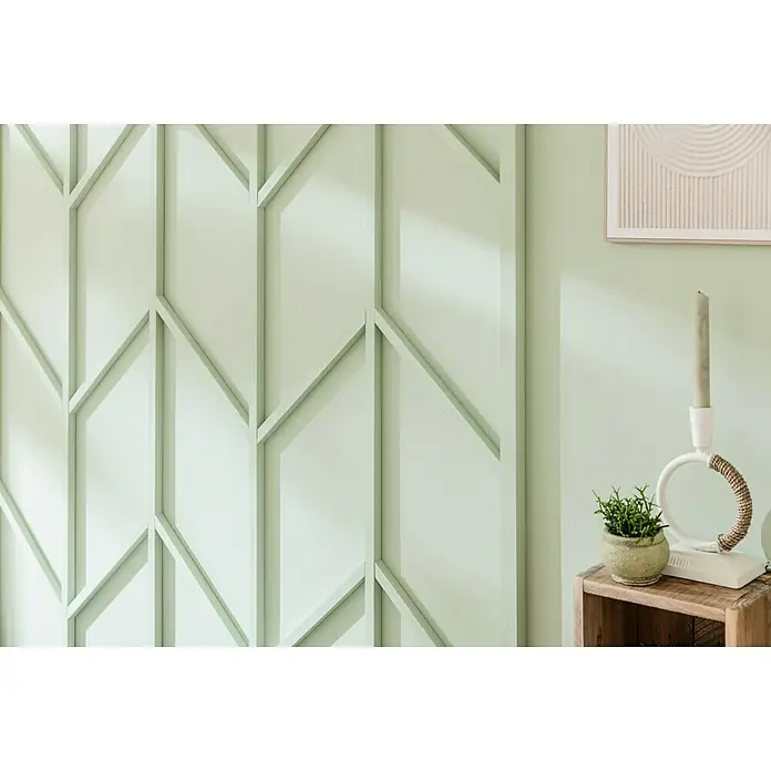 Alpina Wandfarbe Feine FarbenHüterin der Freiheit, Matt, 2,5 l, Konservierungsmittelfrei - Wandpaneele mit geometrischem Design und eine kleine Pflanze auf einem Holzkasten mit einer weißen Kerze, die ein stilvolles Interieur unterstreichen.