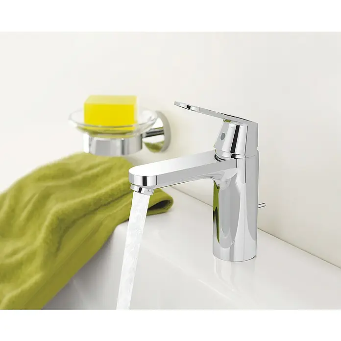 Grohe Eurosmart Cosmopolitan Waschtischarmatur M-Size - Mit Zugstange, Chrom, Glänzend - Nahaufnahme einer modernen Chromarmatur mit fließendem Wasser, ergänzt durch eine Seifenschale und ein grünes Tuch.
