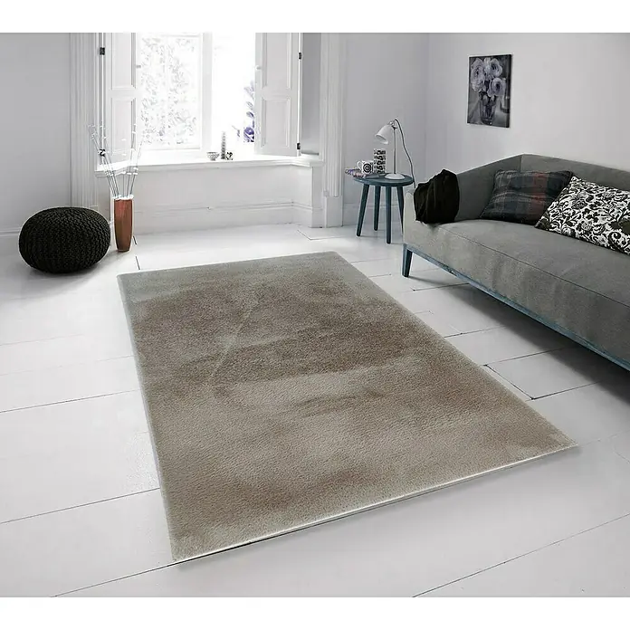 Alfombra de pelo corto Bunny - Taupé, 110 x 60 cm, 100% poliéster - Una alfombra gris está colocada sobre un piso de madera blanca en una sala de estar luminosa. La alfombra suma calidez y confort.