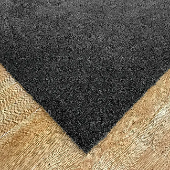 Alfombra de pelo corto Toscana - Gris, 300 x 200 cm, 100% Poliéster - Una alfombra gris con una textura suave se encuentra sobre un piso de madera clara. La alfombra cubre parte del suelo.