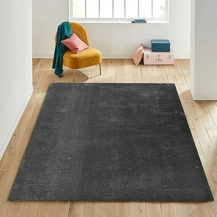 Alfombra de pelo corto Toscana - Gris, 300 x 200 cm, 100% Poliéster - Alfombra gris en un salón con suelo de madera, sillón y decoraciones para un ambiente acogedor.