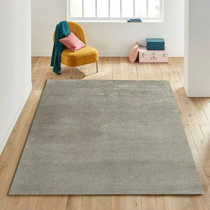Alfombra de pelo corto Toscana - Beige, 300 x 200 cm, 100% Poliéster - Una alfombra gris extendida sobre un piso de madera en una habitación luminosa con una silla amarilla.