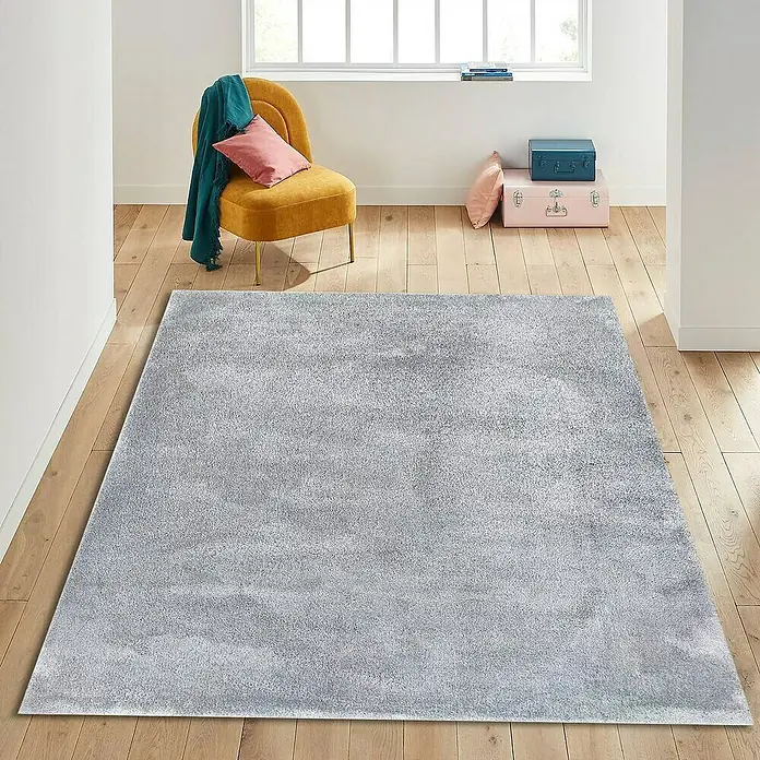 Alfombra de pelo corto Toscana - Plateado, 300 x 200 cm, 100% Poliéster - Una alfombra gris se encuentra sobre un piso de madera clara en una habitación luminosa. La alfombra presenta una textura suave y afelpada para mayor confort.