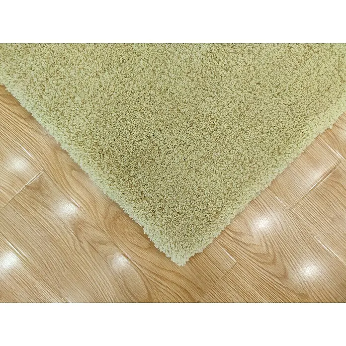Alfombra de pelo corto Hong Kong - Aceite, 115 x 60 cm, Poliéster - Primer plano de una alfombra de pelo largo verde claro colocada sobre un suelo de madera clara, que muestra una textura suave y un ambiente acogedor.