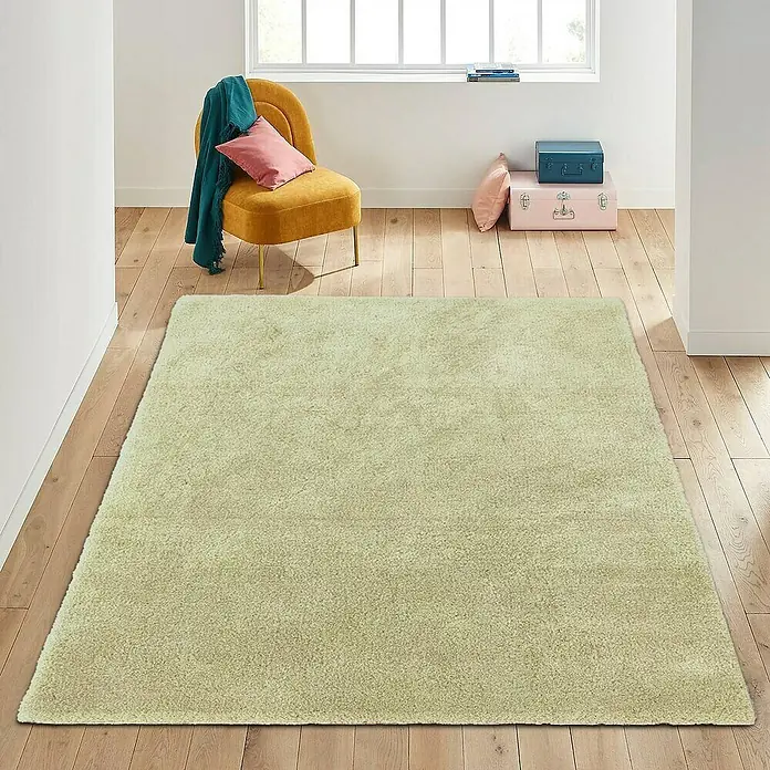 Alfombra de pelo corto Hong Kong - Aceite, 115 x 60 cm, Poliéster - Una alfombra beige en una habitación luminosa con suelos de madera crea un ambiente acogedor. Una silla y accesorios complementan el espacio.