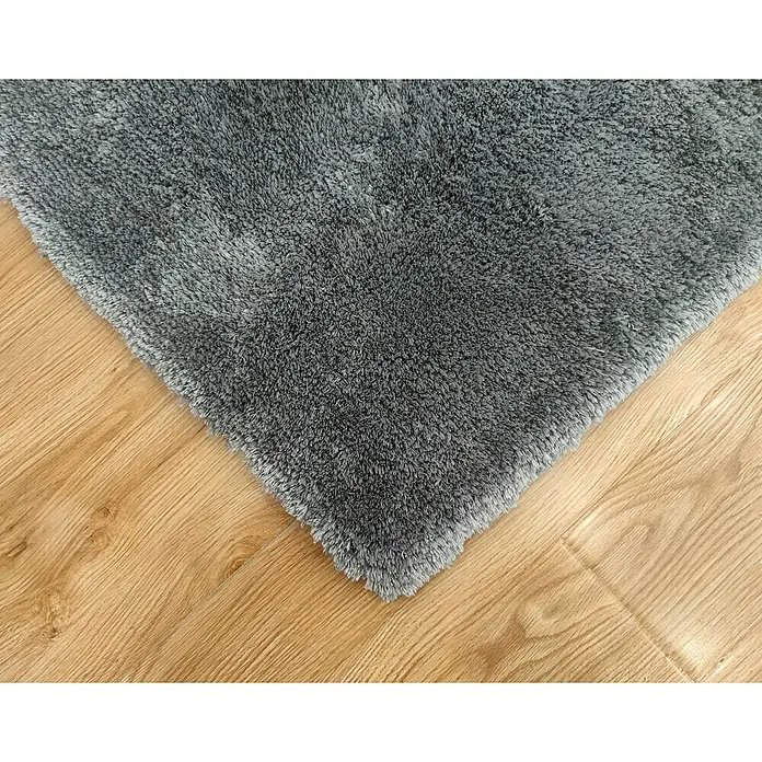 Alfombra de pelo largo Bolonia - Plata, 115 x 60 cm, 100% Poliéster - Primer plano de una alfombra de pelo largo gris sobre un suelo de madera clara, destacando la textura suave de la alfombra y las sutiles variaciones de color.