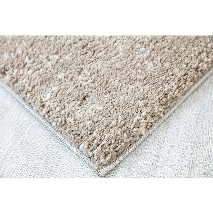 Alfombra de pelo largo Bravo Vigore - Taupe, 180 x 120 cm, Polietileno/Polipropileno - Primer plano de una alfombra beige con un borde sencillo sobre un suelo de madera clara. La alfombra tiene una textura suave.