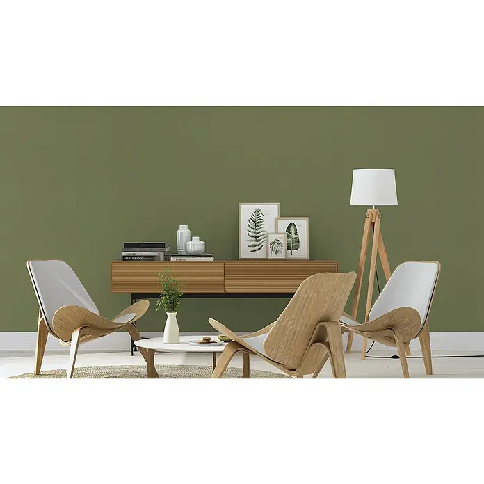 Rasch Tropical House Vliestapete - Moosgrün, Uni, 10,05 x 0,53 m - Das Bild zeigt ein stilvolles Wohnzimmer mit Holzsesseln, einer Kommode und einer Stehlampe. Die grüne Wandfarbe verleiht dem Raum eine natürliche Note.