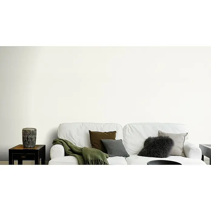 Rasch Tapetenwechsel Vliestapete Classic Style - Weiß, Uni, 10,05 x 0,53 m - Wohnzimmer-Interieur mit einem weißen Sofa, verschiedenen Kissen und einer grünen Decke, die für eine gemütliche Atmosphäre sorgen.