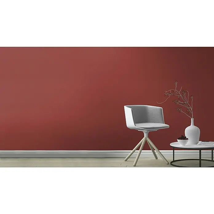 Rasch Tropical House Vliestapete - Ziegelrot, Uni, 10,05 x 0,53 m - Ein heller, moderner Stuhl steht neben einem Beistelltisch mit Deko vor einer roten Wand. Elegantes Design für stilvolle Wohnräume.