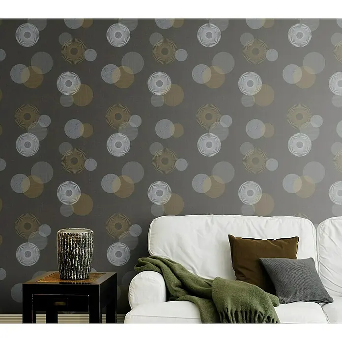 Rasch Color your life Vliestapete Kreise - Anthrazit, Grafisch, 10,05 x 0,53 m - Nahaufnahme einer grauen gemusterten Wand mit einem weißen Sofa, Kissen und einer grünen Decke im Vordergrund.
