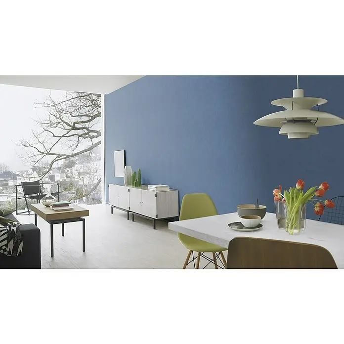Rasch Wall Textures VI Vliestapete Uni - Taubenblau, Uni, 10,05 x 0,53 m - Ein helles Interieur mit einem markanten Couchtisch und einem eleganten weißen Sideboard vor einer blauen Wand.
