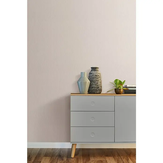 Rasch Color your life Vliestapete Längsuni - Beigerosa, Uni, 10,05 x 0,53 m - Stilvolle graue Kommode mit Holzplatte, verziert mit Vasen und Pflanze, vor einer zartrosa Wand für ein elegantes Ambiente.