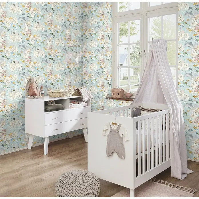 Rasch Kids World Vliestapete Fische - Hellblau, Tieroptik, 10,05 x 0,53 m - Ein helles Kinderzimmer mit einem weißen Kinderbett mit Baldachin, einer Kommode und einem Pouf. Die Wände sind mit einem Unterwasser-Motiv tapeziert.