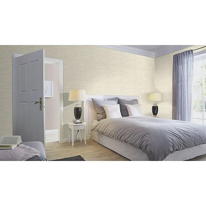 Rasch Factory V Vliestapete Beton - Hellbeige, Steinoptik, 10,05 x 0,53 m - Dieses Schlafzimmer zeigt eine mit Ziegeln verzierte Wand, ein großes Bett und ein offenes Badezimmer mit sanften Pastelltönen.