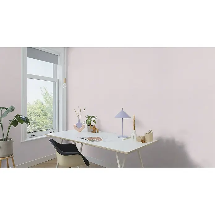 Rasch Country Charme Vliestapete Textil-Uni - Hellrosa, Uni, 10,05 x 0,53 m - Ein helles Heimbüro mit einem Schreibtisch mit Lampe, Pflanzen und Dekor, alles vor einer hellrosa Wand, die eine ruhige Arbeitsatmosphäre bietet.