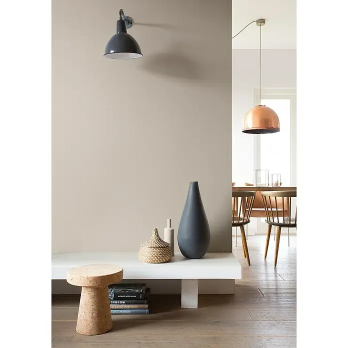 Rasch Color your life Vliestapete Struktur-Uni - Hellbeige, Uni, 10,05 x 0,53 m - Eine Inneneinrichtung mit einer grauen Wandleuchte, einer kupferfarbenen Hängelampe und einer Komposition aus Vasen und Büchern auf einem weißen Regal.