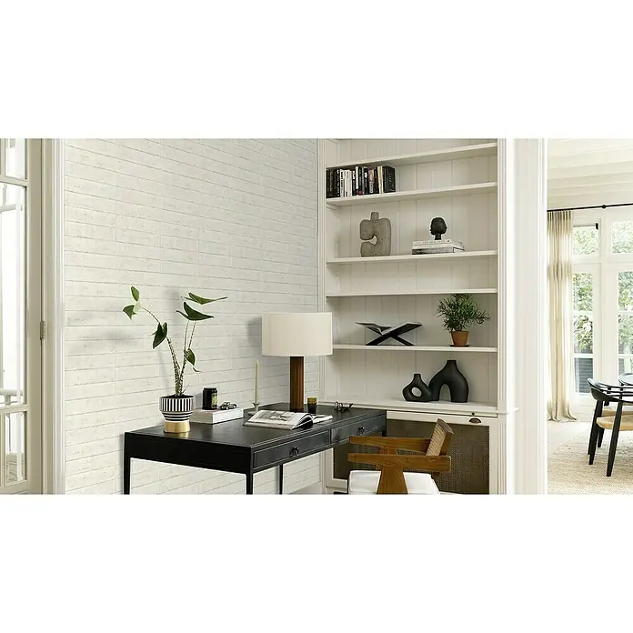 Rasch Factory V Vliestapete Beton - Kalkstein, Steinoptik, 10,05 x 0,53 m - Elegantes Heimbüro mit schwarzem Schreibtisch, stilvollem Holzstuhl und einem weißen Bücherregal, dekoriert mit Pflanzen und moderner Kunst.