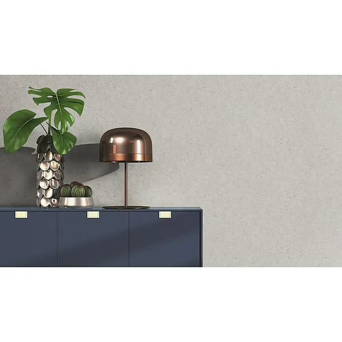 Rasch Factory V Vliestapete Beton-Uni - Mittelgrau, Uni, 10,05 x 0,53 m - Elegantes Sideboard in Dunkelblau mit dekorativer Tischlampe, Vase und Pflanze vor einer grauen Wand, das die perfekte Deko für jeden Raum darstellt.