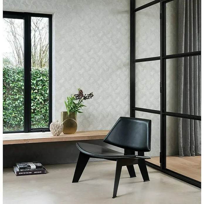 Rasch Sky Lounge Vliestapete Graphik - Platingrau, Grafisch, 10,05 x 0,53 m - Elegantes Interieur mit einem schwarzen Ledersessel vor einer strukturierten Wand, ergänzt durch natürliche Elemente und moderne Akzente.