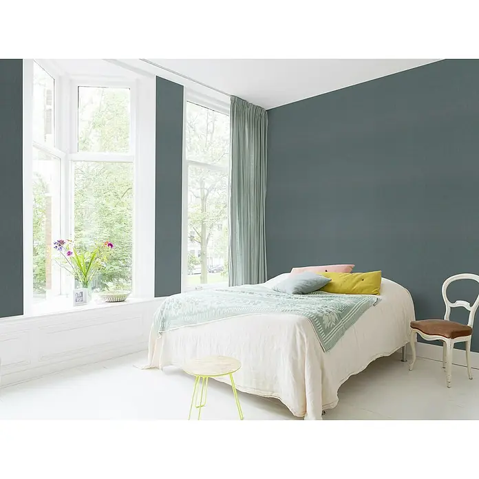 Rasch Sky Lounge Vliestapete Metallic-Uni - Blaugrau, Uni, 10,05 x 0,53 m - Schlafzimmer mit großem Fenster, Bett mit bunten Kissen, kleiner Tisch und Stuhl, die eine entspannte Atmosphäre schaffen.\n