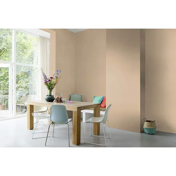Rasch Symphony Vliestapete Leinen-Uni - Dunkelbeige, Uni, 10,05 x 0,53 m - Innenaufnahme eines Esszimmers mit Holztisch, Stühlen, Blumen, Sitzbank mit Kissen und einem dekorativen Korb vor einer beigen Wand.