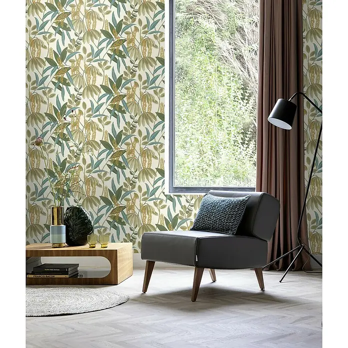 Rasch Country Charme Vliestapete Blätter - Moosgrün, Floral, 10,05 x 0,53 m - Ein stilvoller Sessel mit floral gemusterter Tapete, ergänzt durch eine Stehlampe und einen Holztisch mit Deko-Elementen, schafft eine einladende Atmosphäre.