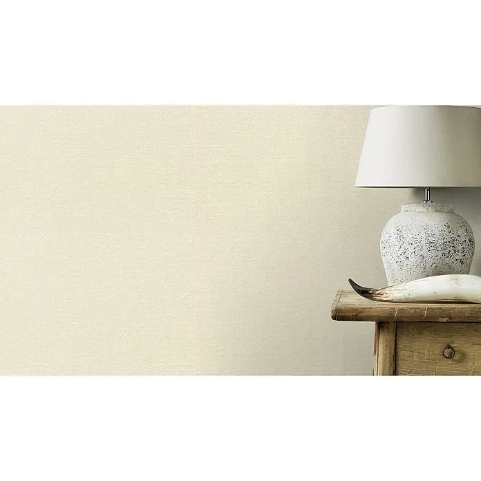 Rasch Color your life Vliestapete Uni-Struktur - Braunbeige, Uni, 10,05 x 0,53 m - Einrichtungsaufnahme mit Lampe, Horn und Nachttisch vor einer schlichten, cremefarbenen Wand. Fokus liegt auf der dekorativen Lampe.